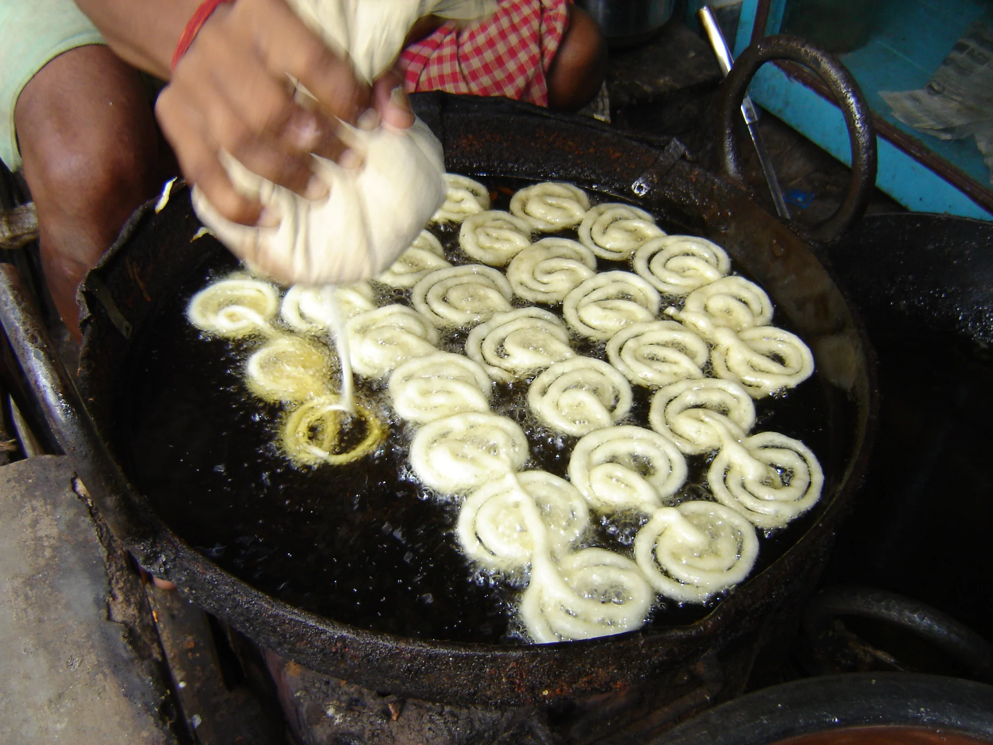 A vendor preparing jalebi by pouring batter in spiral patterns into hot oil