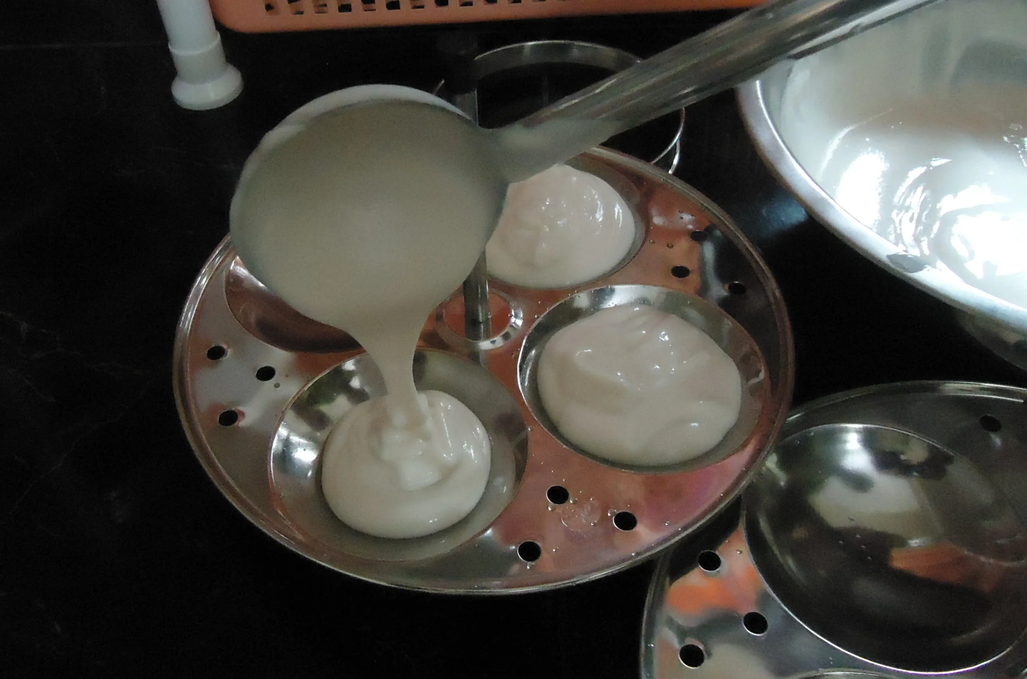Idli batter being poured into traditional idli molds